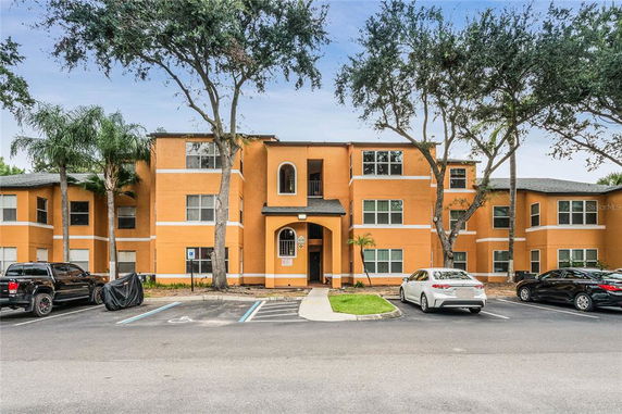 Front view of a three-story apartment building with orange facade and parking area.