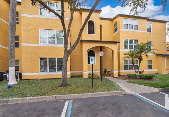 Front view of a multi-story yellow apartment building with an arched entrance and multiple windows.