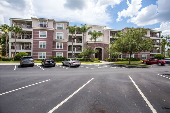 Front view of a four-story apartment building with balconies and a parking area in front.