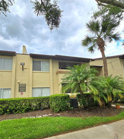 Front view of a two-story apartment building with beige exterior and palm trees in front.