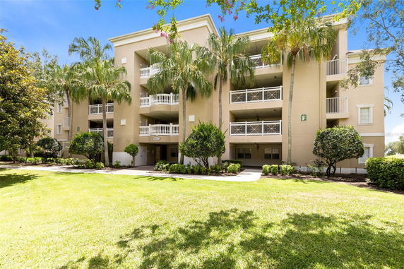 Front view of a multi-story apartment building with balconies and palm trees in front.