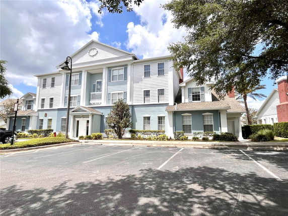 Front view of a multi-story residential building with white and blue facade, featuring large windows and a gabled roof.