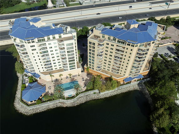 Aerial view of two high-rise residential buildings with blue roofs near a highway and river.