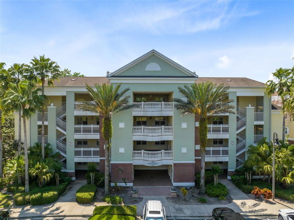 Front view of a three-story residential building with balconies and palm trees.