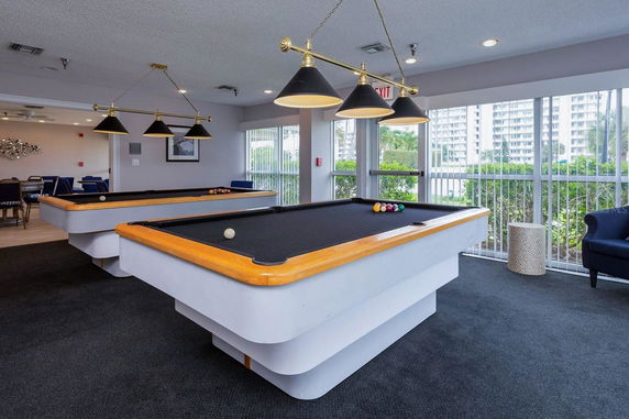 Indoor billiards room with multiple pool tables and seating area.