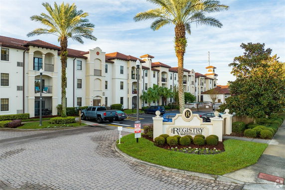 Front view of a multi-story apartment building with a landscaped entrance and parking area.