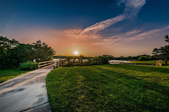 Wide angle view of a sunset with a path and bridge leading towards a body of water, surrounded by greenery.