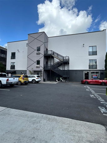 Front view of a modern three-story building with an external staircase and parking area.