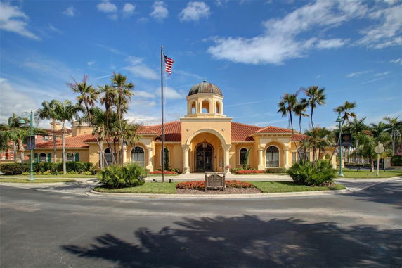 Front view of a building with a central dome and arches, featuring a flagpole and palm trees.