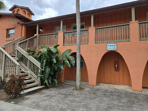 Front view of a two-story building with an external staircase and arched entrances.