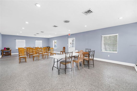 Interior view of a room with multiple chairs and tables, blue walls, and windows with blinds.
