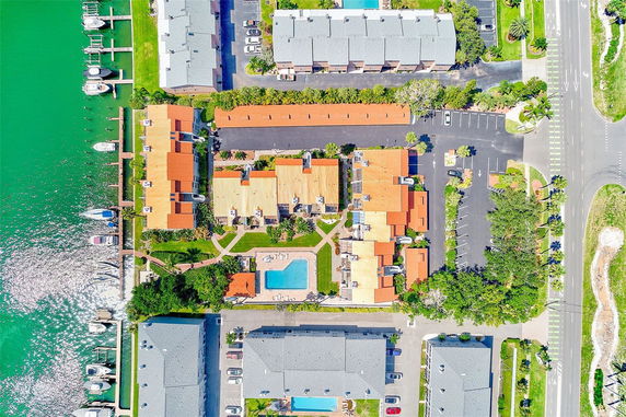 Aerial view of a residential complex with multiple buildings, a swimming pool, parking areas, and a waterfront with boats.
