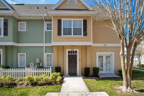 Front view of a townhouse with a beige and green facade and a small white picket fence.