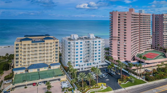 Front view of several beachfront high-rise buildings with balconies and parking spaces.