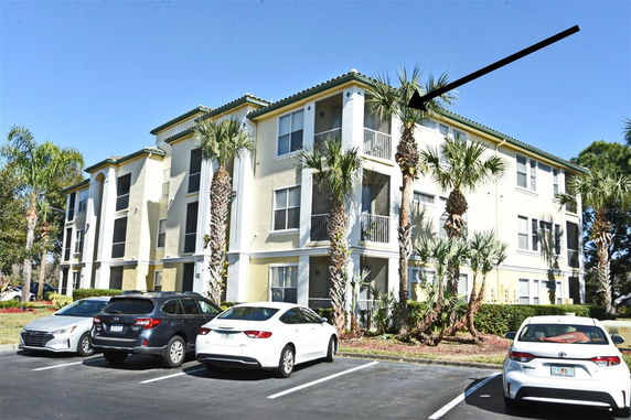 Front view of a multi-story apartment building with balconies and parked cars.