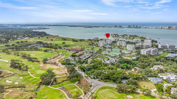 Aerial panoramic view of residential buildings near a waterfront, surrounded by green landscapes and a golf course.