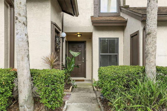 Front entrance of a townhouse with a brown door and surrounding plants.