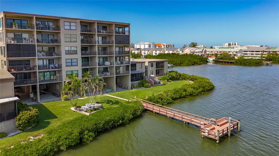 Front view of a multi-story residential building by the water with a dock extending over the river.