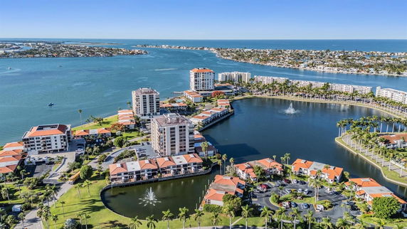 Panoramic view of residential buildings near water with a fountain and surrounding landscape.