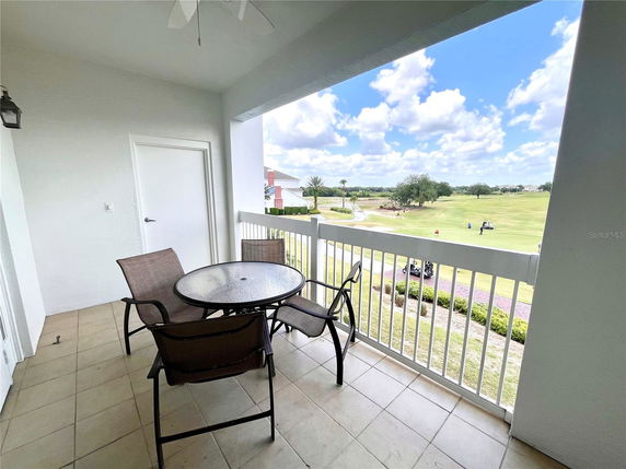 Balcony view overlooking a golf course with a table and chairs.