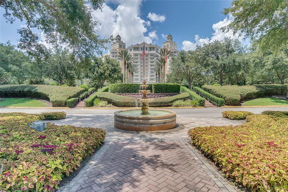 Front view of a multi-story building with decorative towers and landscaping, featuring a fountain.