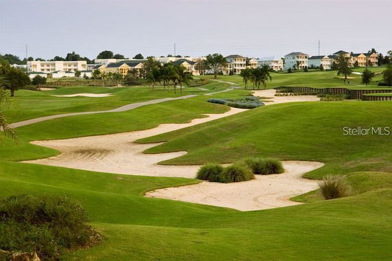 Landscaped golf course with sand traps and nearby residential buildings in the background.