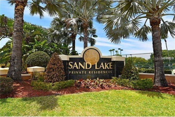 Entrance sign for Sand Lake Private Residences surrounded by palm trees and landscaped greenery.