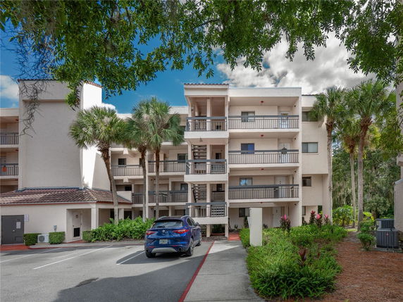 Front view of a multi-story apartment building with balconies and a parking area