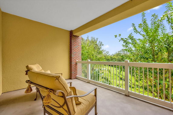 Balcony with yellow cushions overlooking greenery and a clear sky.