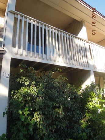 View of a house with a balcony and bushes in the foreground.