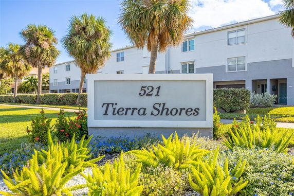 Front view of a multi-story building with a landscaped foreground and a sign reading 'Tierra Shores 521'.