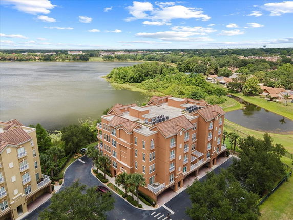 Aerial view of a multi-story building with a rooftop featuring air conditioning units, situated near a lake.