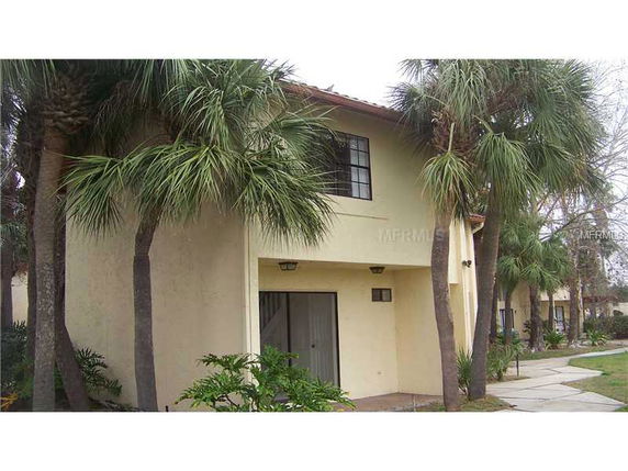 Front view of a two-story house with a side entrance and palm trees.
