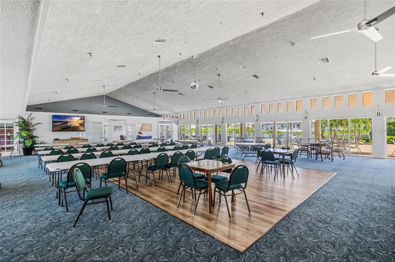 Spacious indoor clubhouse with tables and chairs, large windows and ceiling fans.
