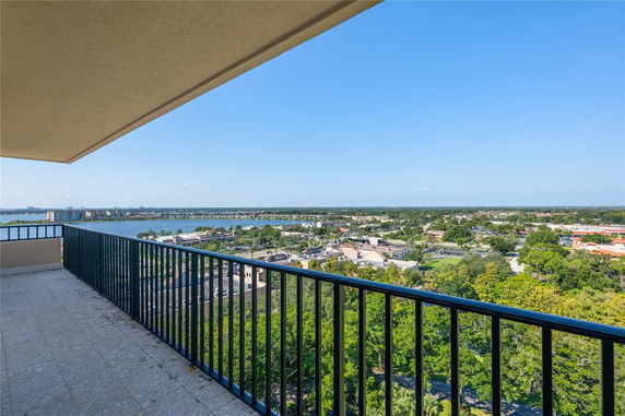 Panoramic view from a high-rise balcony overlooking a cityscape and water body.