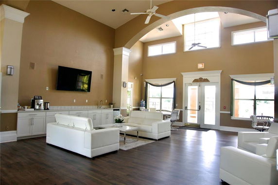Interior of a clubhouse with sofas, a TV, and large windows.
