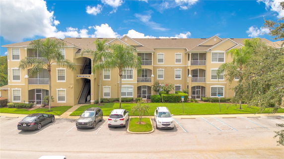 Front view of a multi-story apartment building with balconies and a parking area.