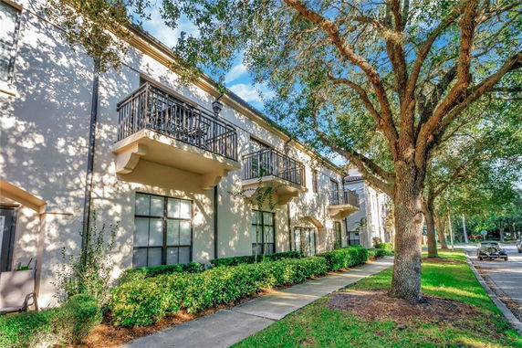 Front view of a two-story building with balconies and a sidewalk lined with trees.