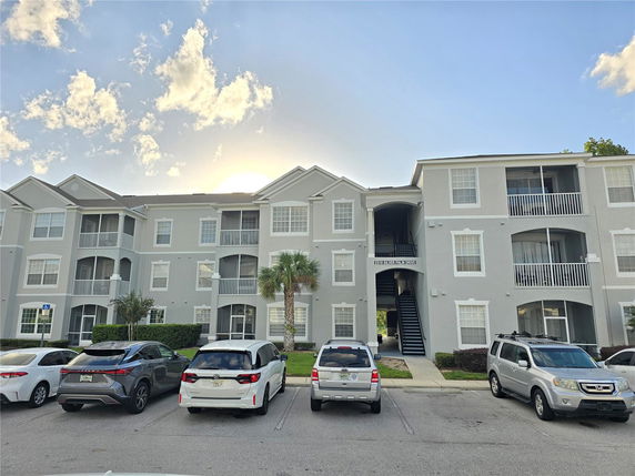 Front view of an apartment building with multiple balconies and parking area.