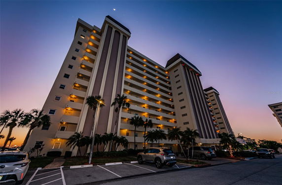 Front view of a multi-story apartment building with balconies and evening lights.