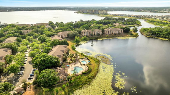 Aerial panoramic view of a residential complex with multiple buildings, a swimming pool, and surrounded by water and greenery.