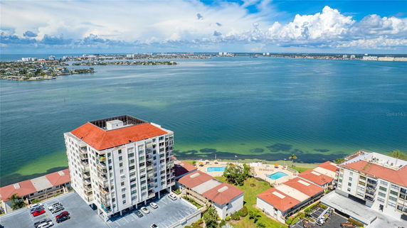 Aerial view of a residential building with a red roof and swimming pool, overlooking a large body of water.