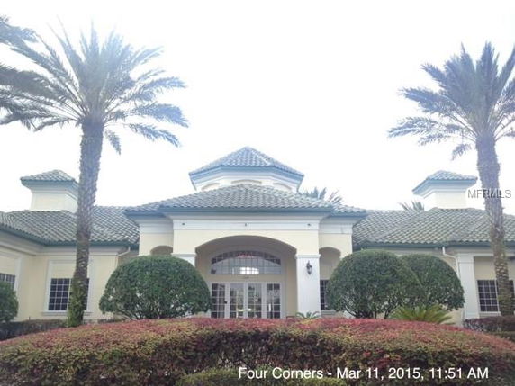 Front view of a house with a green tiled roof and arched entrance surrounded by manicured shrubs and palm trees.