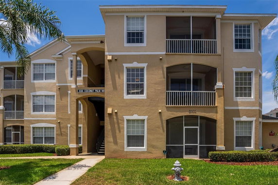 Front view of a multi-story beige apartment building with white trim and balconies.