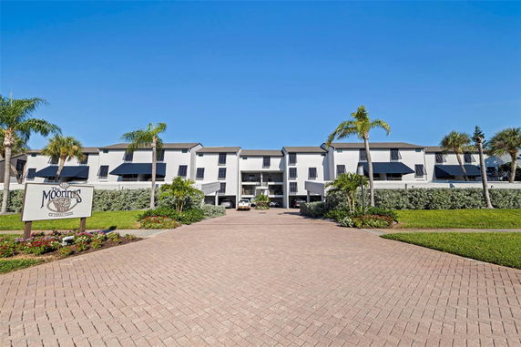 Front view of a white multi-story residential building with black awnings and a paved driveway.
