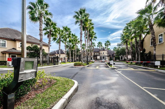 Front view of a gated residential entrance with palm trees and surrounding buildings.