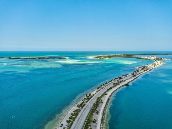Aerial view of a coastal road surrounded by blue ocean waters and small islands in the distance.
