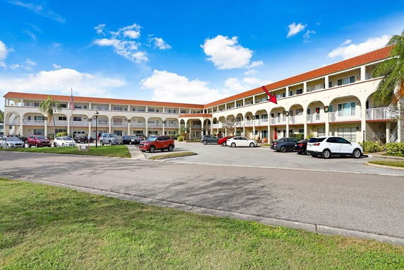 Front view of a multi-story building with white balconies and parked cars.