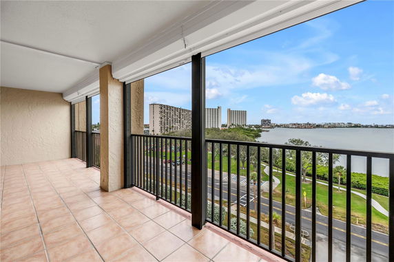 Covered balcony with railing offering a panoramic view of high-rise buildings and a water body.
