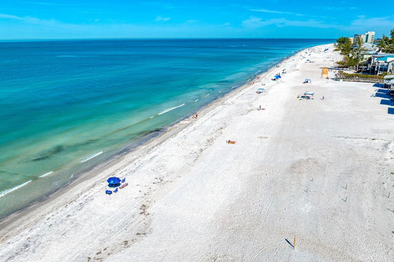 Panoramic view of a sandy beach with turquoise waters and scattered beachgoers under umbrellas.